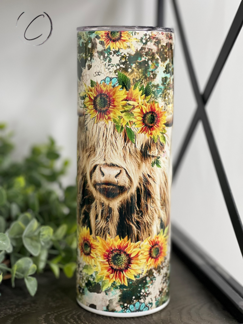 A stylish 20oz skinny tumbler featuring a Highland cow surrounded by vibrant sunflowers, perfect for drinks on the go.