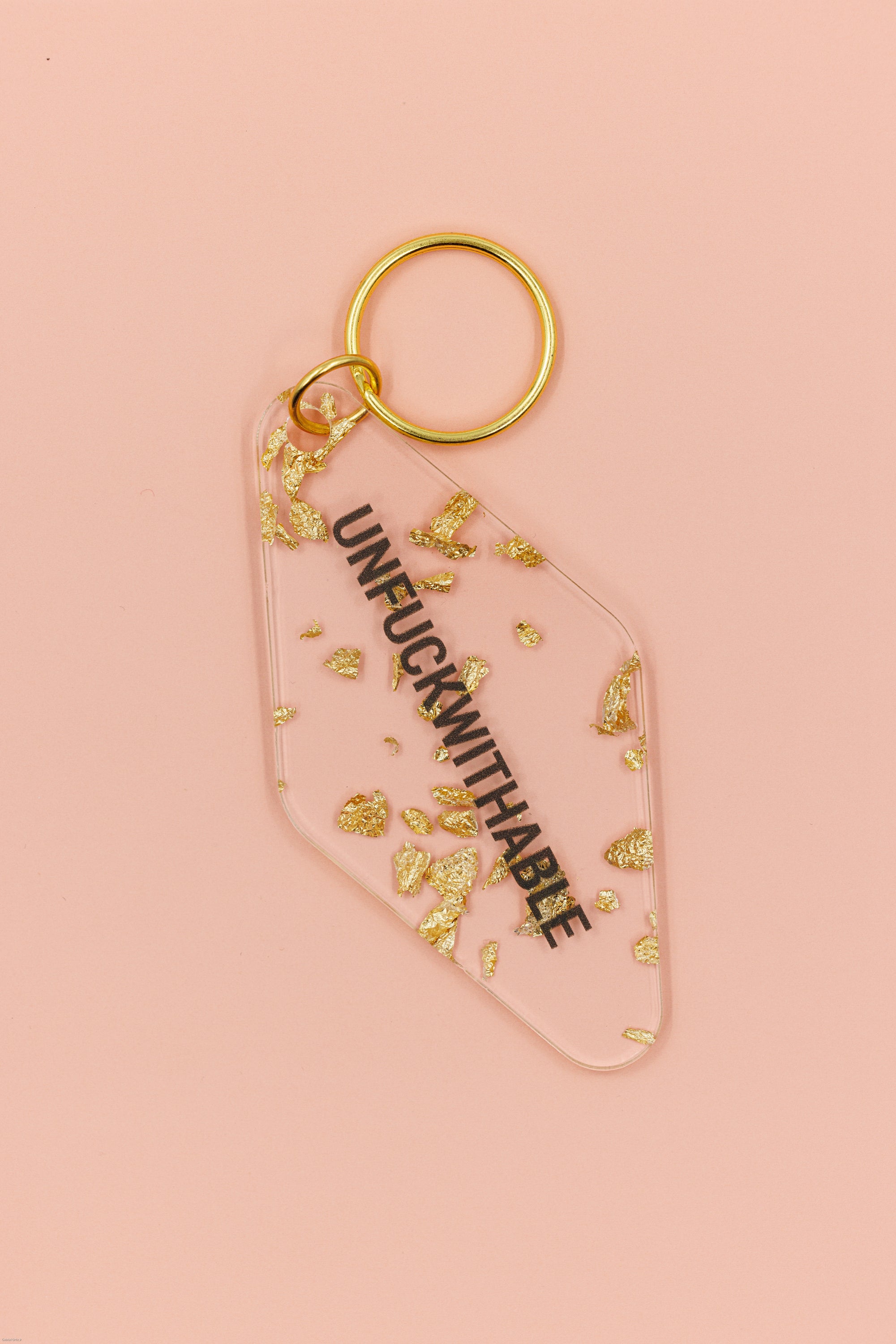 Clear keychain with gold leaf accents and gold hardware, featuring the text 'UNFUCKWITHABLE'.