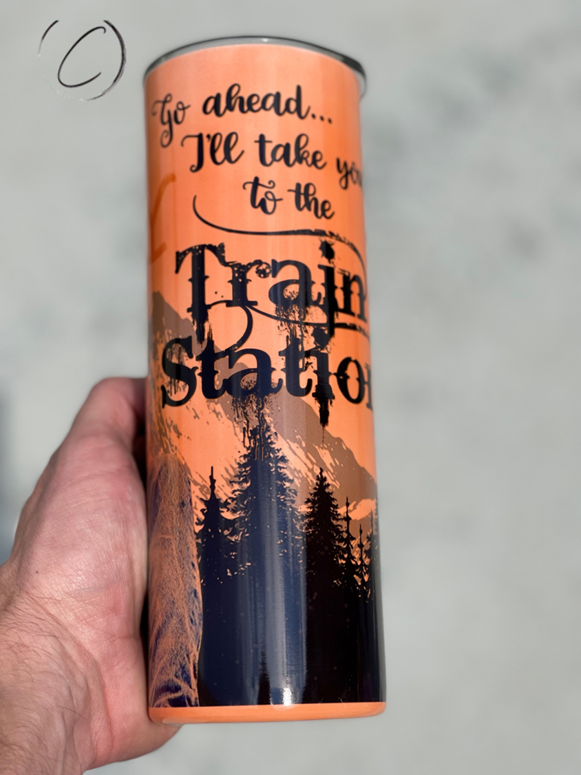 Yellowstone Train Station 20oz UV Orange Skinny Tumbler with a vibrant color-changing effect in sunlight, featuring a reusable straw.