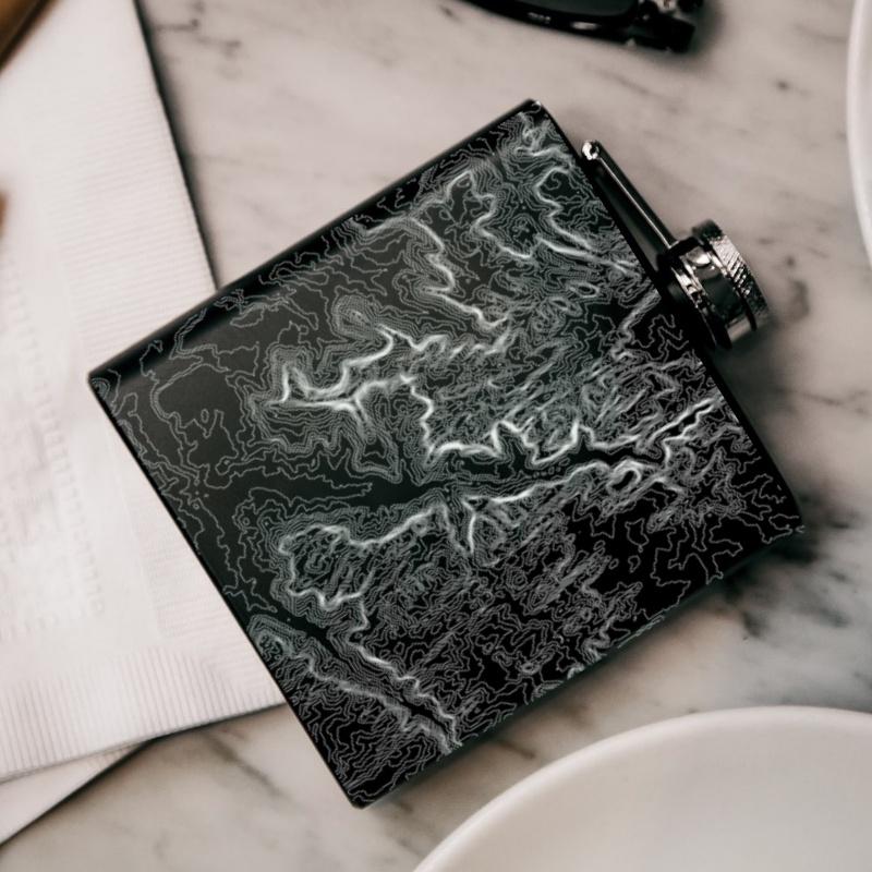 Custom engraved matte black hip flask featuring a detailed map of Zion National Park, Utah, with coordinates, accompanied by a canvas bag and funnel.