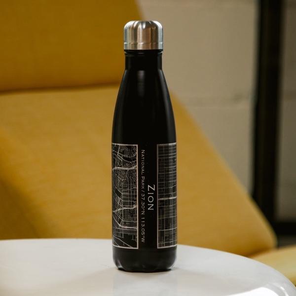 Matte black insulated stainless steel bottle featuring a custom engraved map of Zion National Park, Utah, with coordinates.