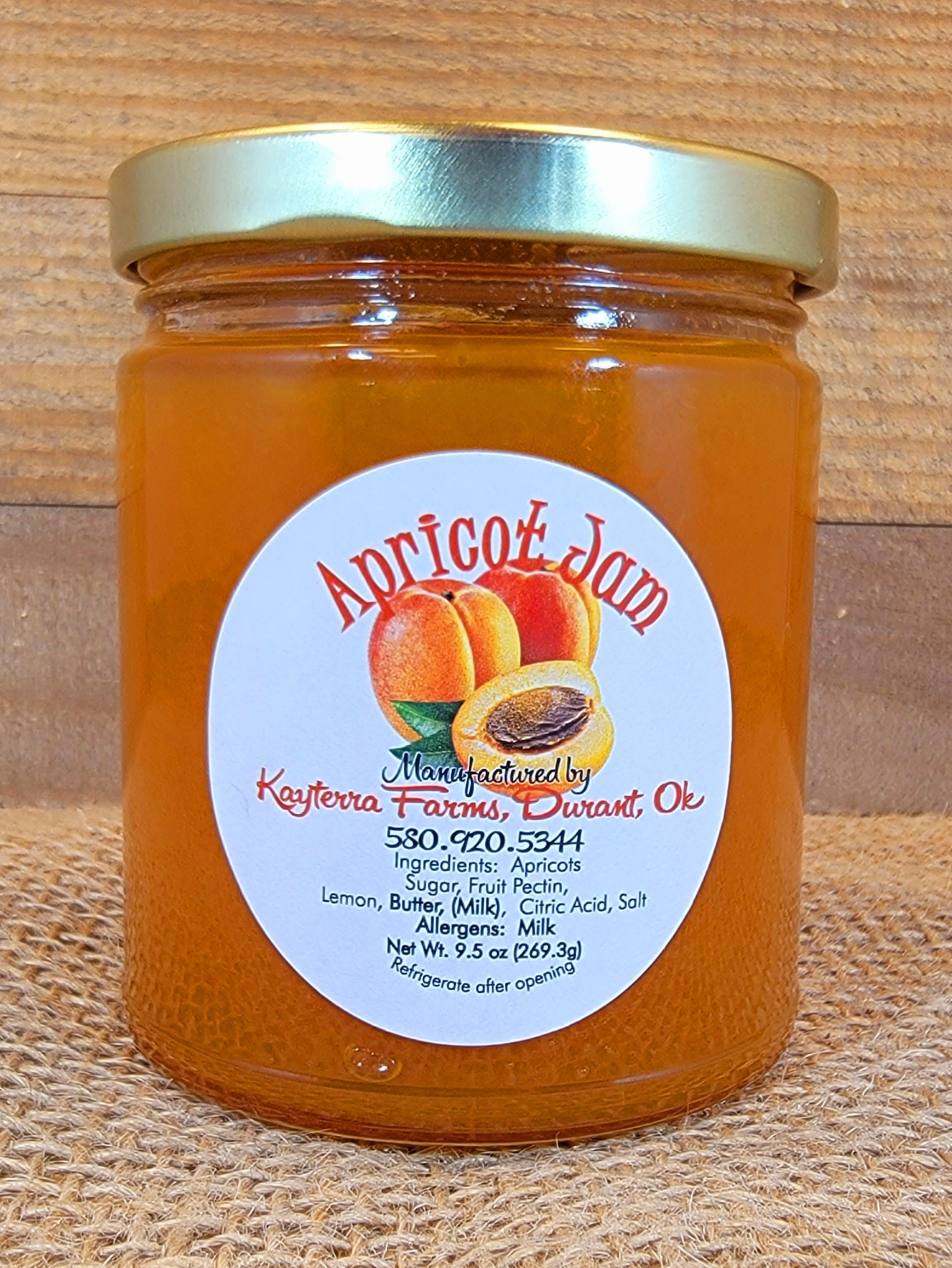 A jar of homemade apricot jam with a golden hue, surrounded by fresh apricots and a rustic spoon.