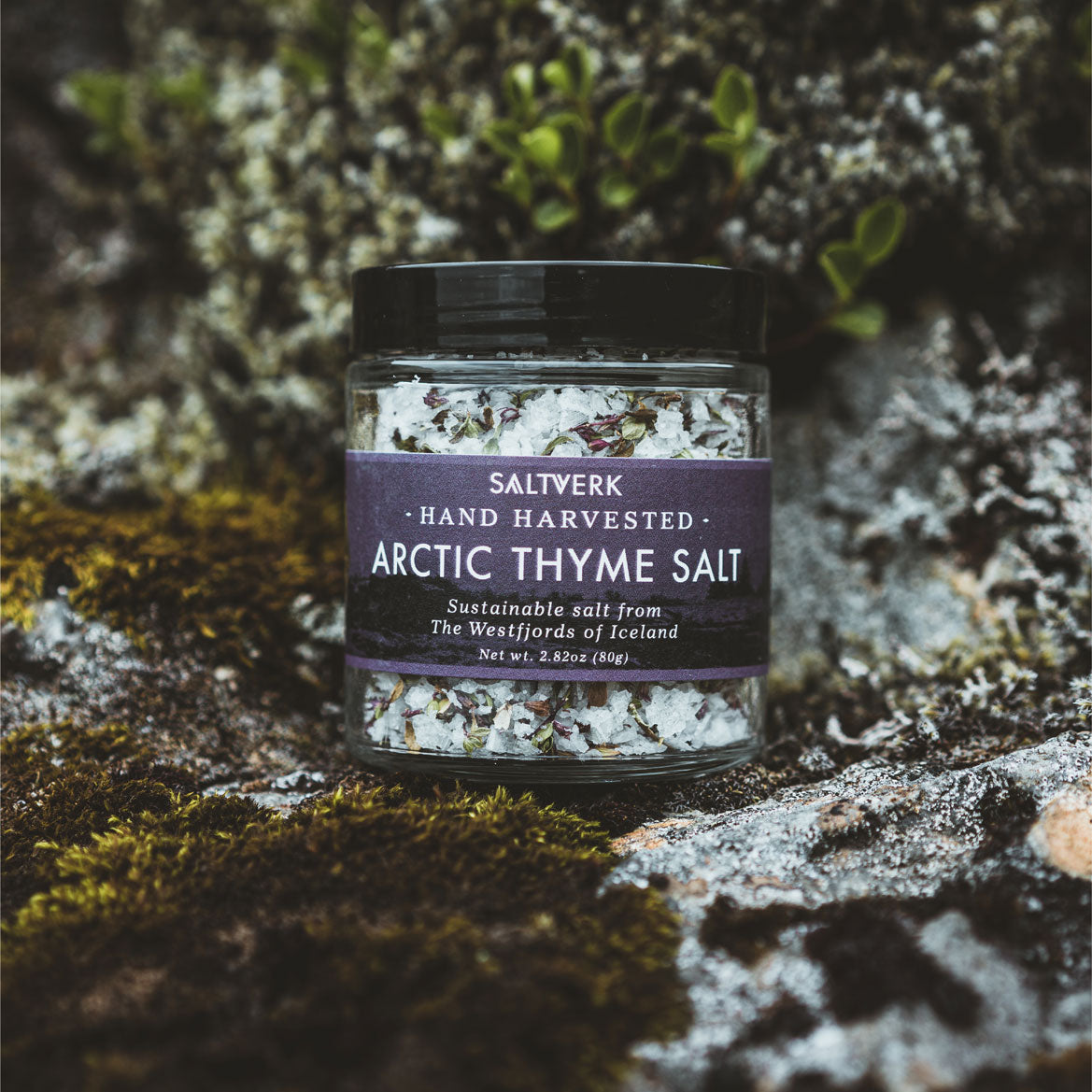 A jar of Arctic Thyme Salt showcasing wild Icelandic thyme and flaky sea salt, set against a rustic wooden background.