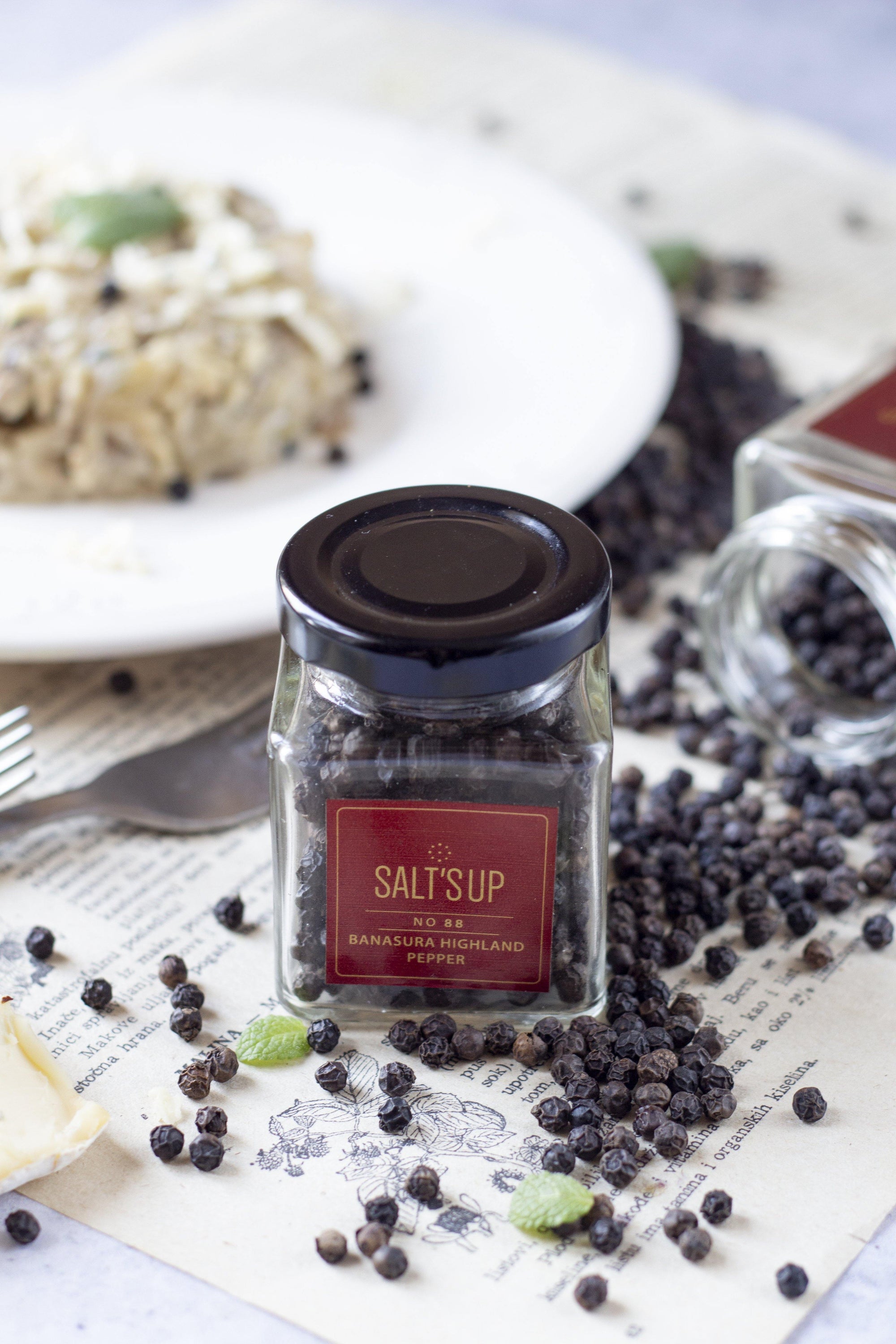 A glass jar containing Banasura Highland pepper, showcasing its rich, dark berries and elegant packaging.