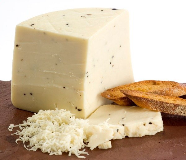 A round wheel of Black Truffle Goat cheese with a creamy texture, garnished with black truffle shavings, set against a rustic wooden background.