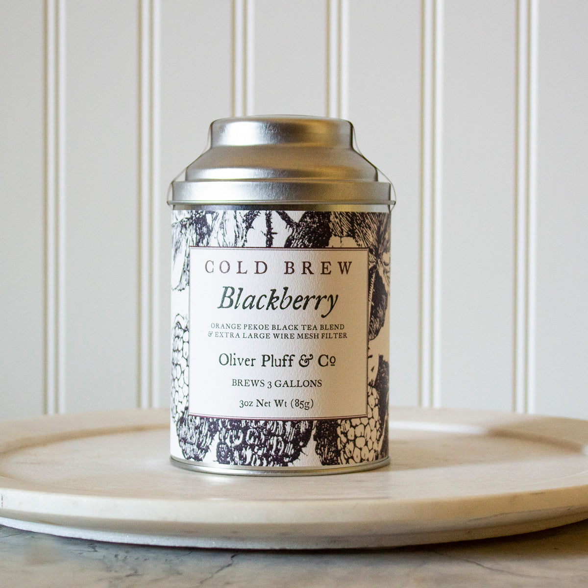 A tin of Blackberry Cold Brew tea with a large wire mesh brewing ball, showcasing the blend of black tea and blackberry leaves.