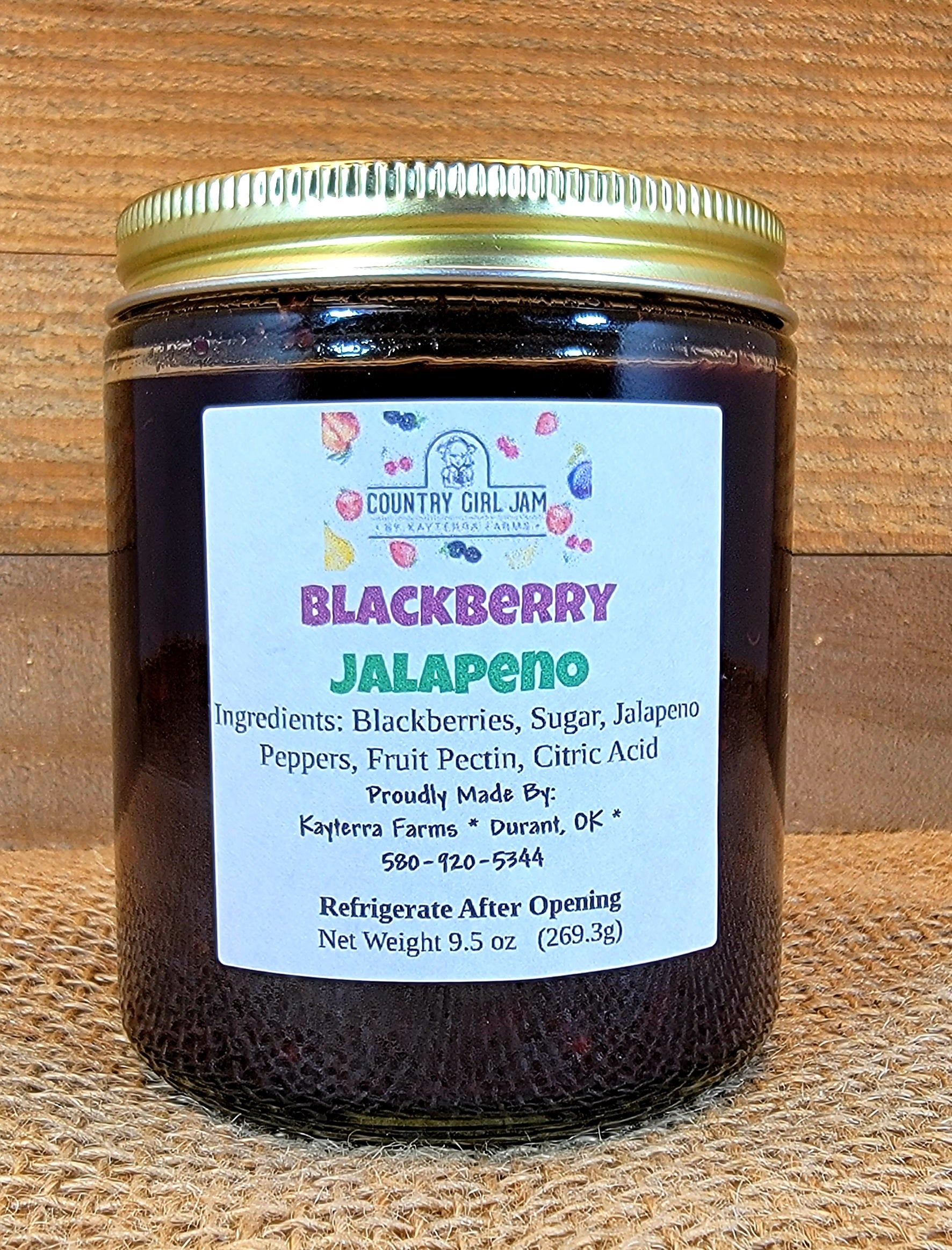 A jar of Blackberry Jalapeno jam with blackberries and jalapenos in the background, showcasing its unique flavor.