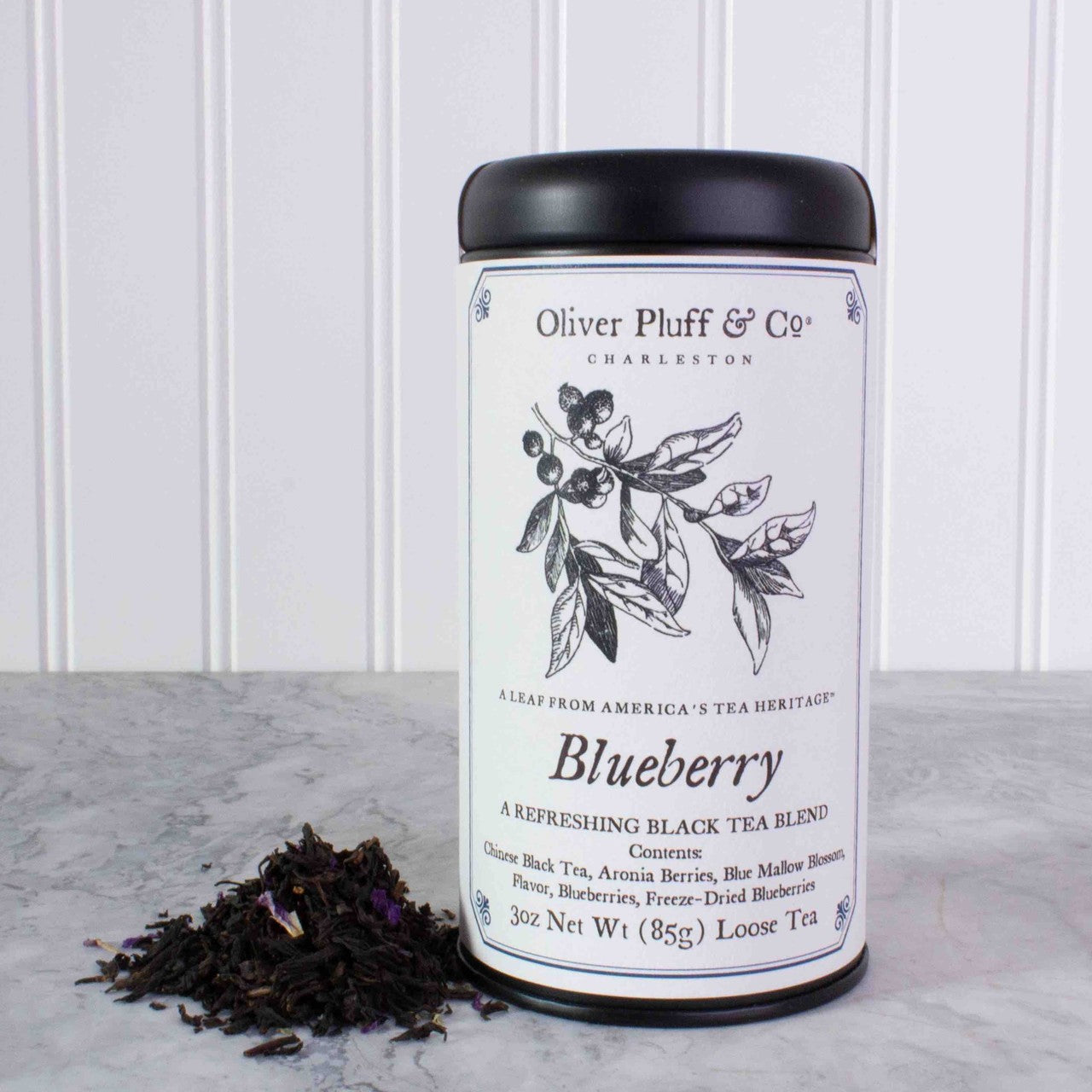 A stylish matte black tin containing Blueberry Loose Tea, showcasing the vibrant colors of the tea leaves and blueberries.