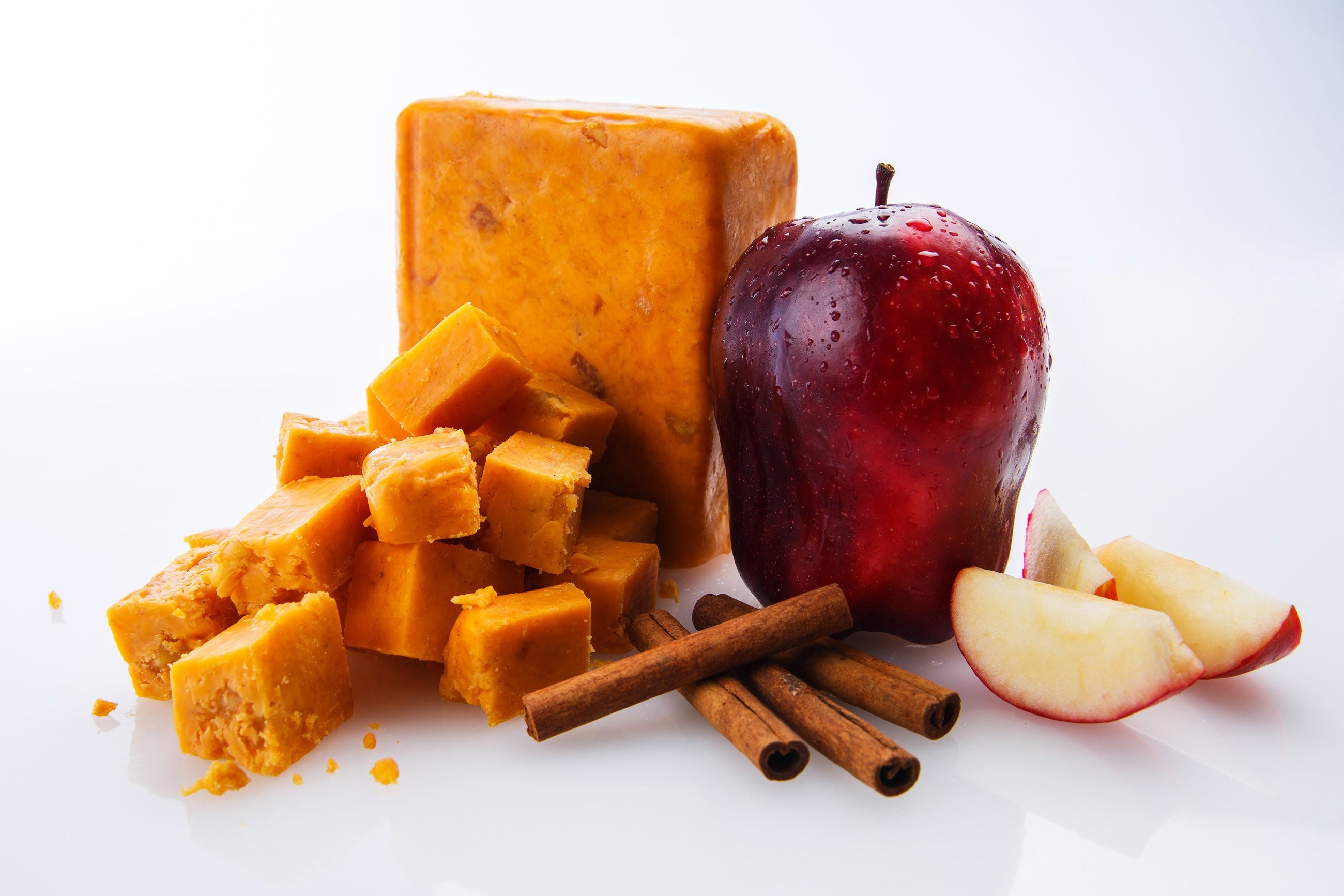 A block of Cinnamon Apple Cheddar cheese with visible apple chunks and a sprinkle of cinnamon, showcasing its unique flavor profile.