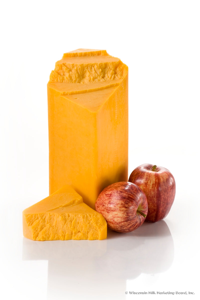 A block of Cinnamon Apple Cheddar cheese with visible apple chunks and a sprinkle of cinnamon, showcasing its unique flavor profile.