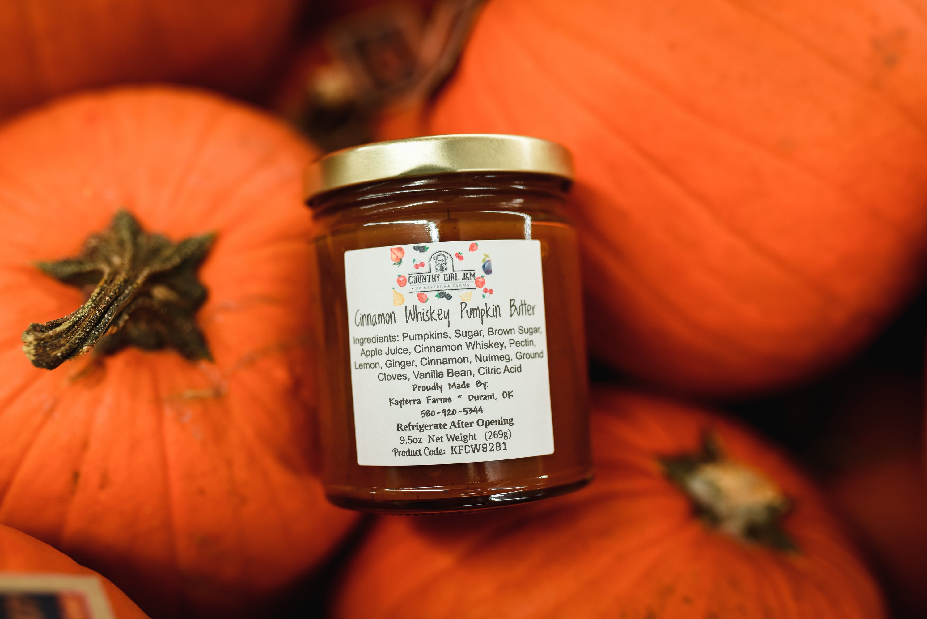 A jar of Cinnamon Whiskey Pumpkin Butter with a rustic label, surrounded by cinnamon sticks and pumpkin decorations, showcasing its festive appeal.