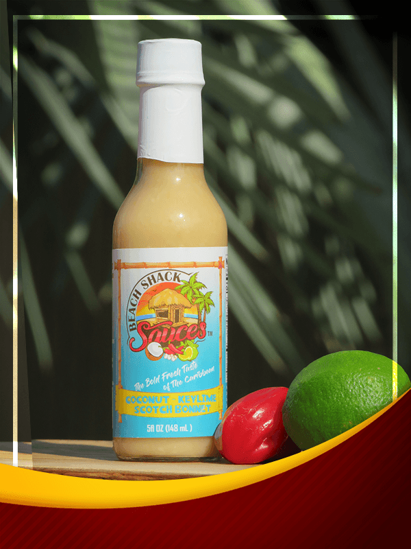 A bottle of Coconut Key Lime Scotch Bonnet sauce with tropical ingredients in the background, showcasing its vibrant color and texture.