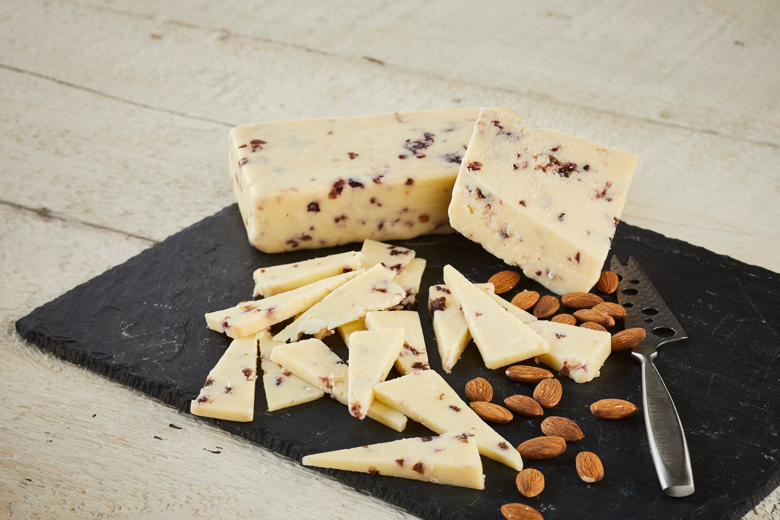 A block of Cranberry Infused Cheddar cheese showcasing its creamy texture and visible cranberry pieces, perfect for cheese lovers.