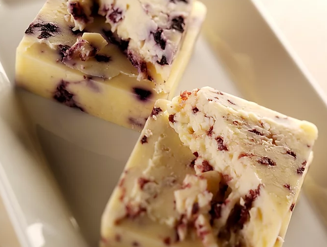 A block of Cranberry Infused Cheddar cheese showcasing its creamy texture and visible cranberry pieces, perfect for cheese lovers.