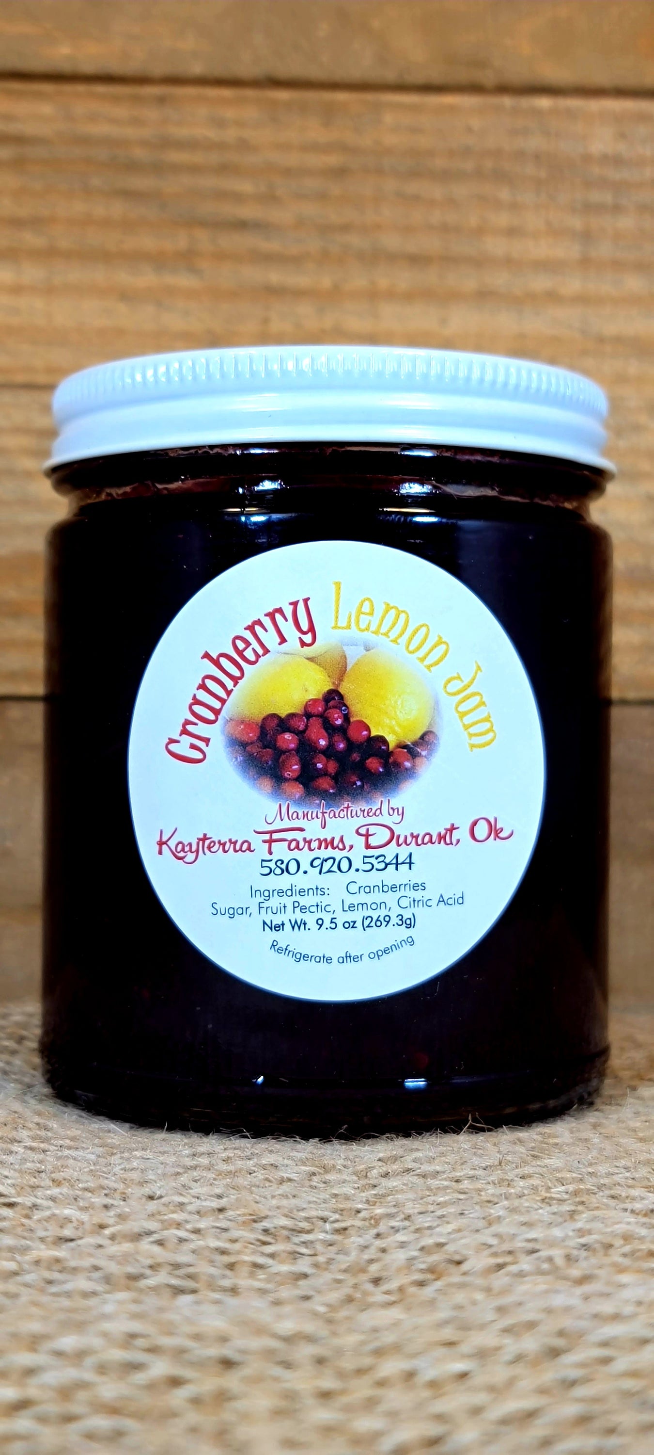 A jar of Cranberry Lemon sauce with cranberries and lemons in the background, showcasing its vibrant color and texture.