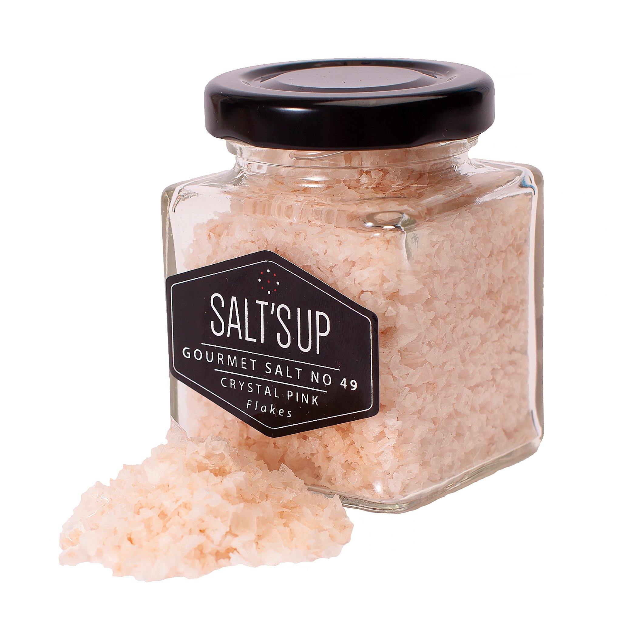 A glass jar filled with CRYSTAL PINK salt flakes, showcasing their beautiful pink color and flaky texture.