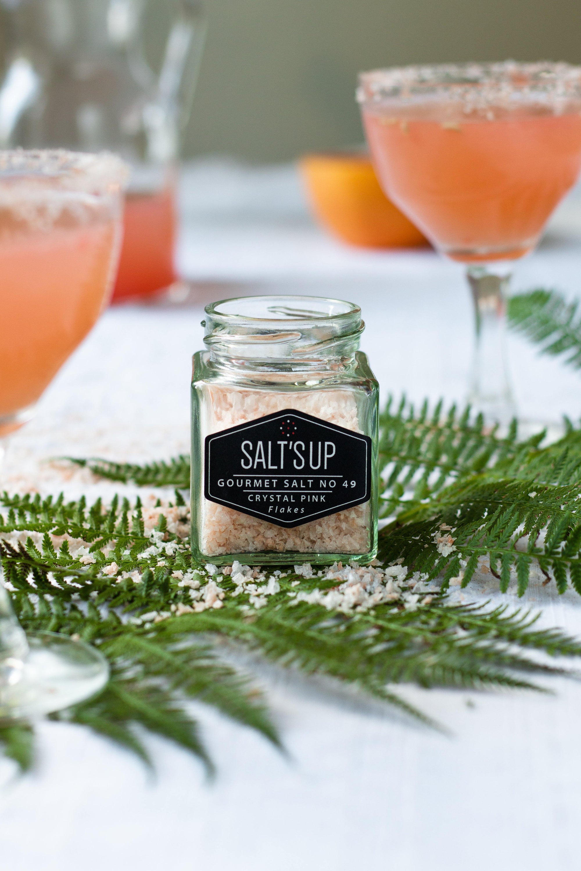 A glass jar filled with CRYSTAL PINK salt flakes, showcasing their beautiful pink color and flaky texture.