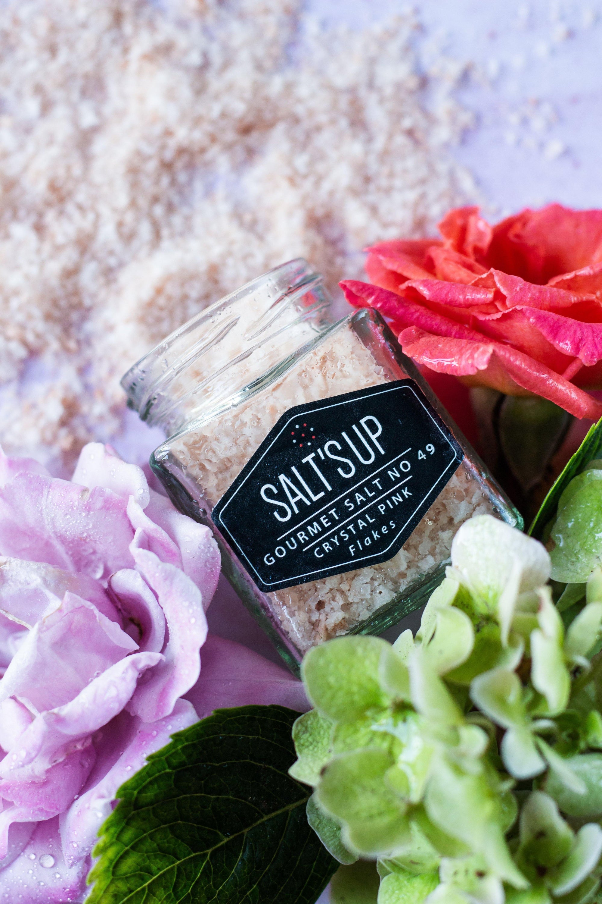 A glass jar filled with CRYSTAL PINK salt flakes, showcasing their beautiful pink color and flaky texture.