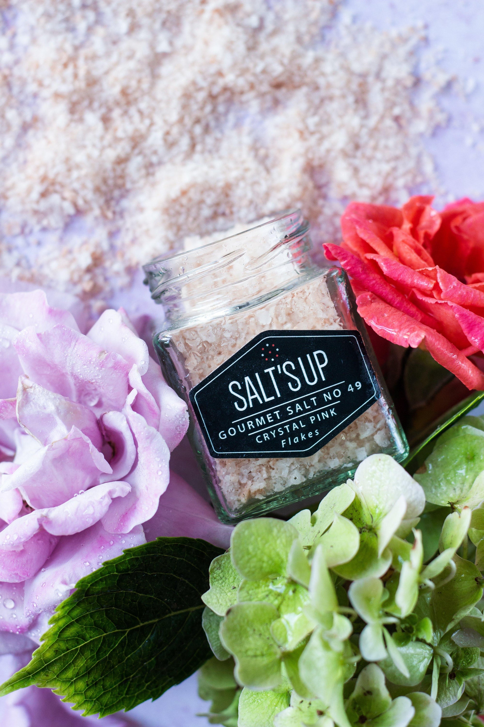 A glass jar filled with CRYSTAL PINK salt flakes, showcasing their beautiful pink color and flaky texture.