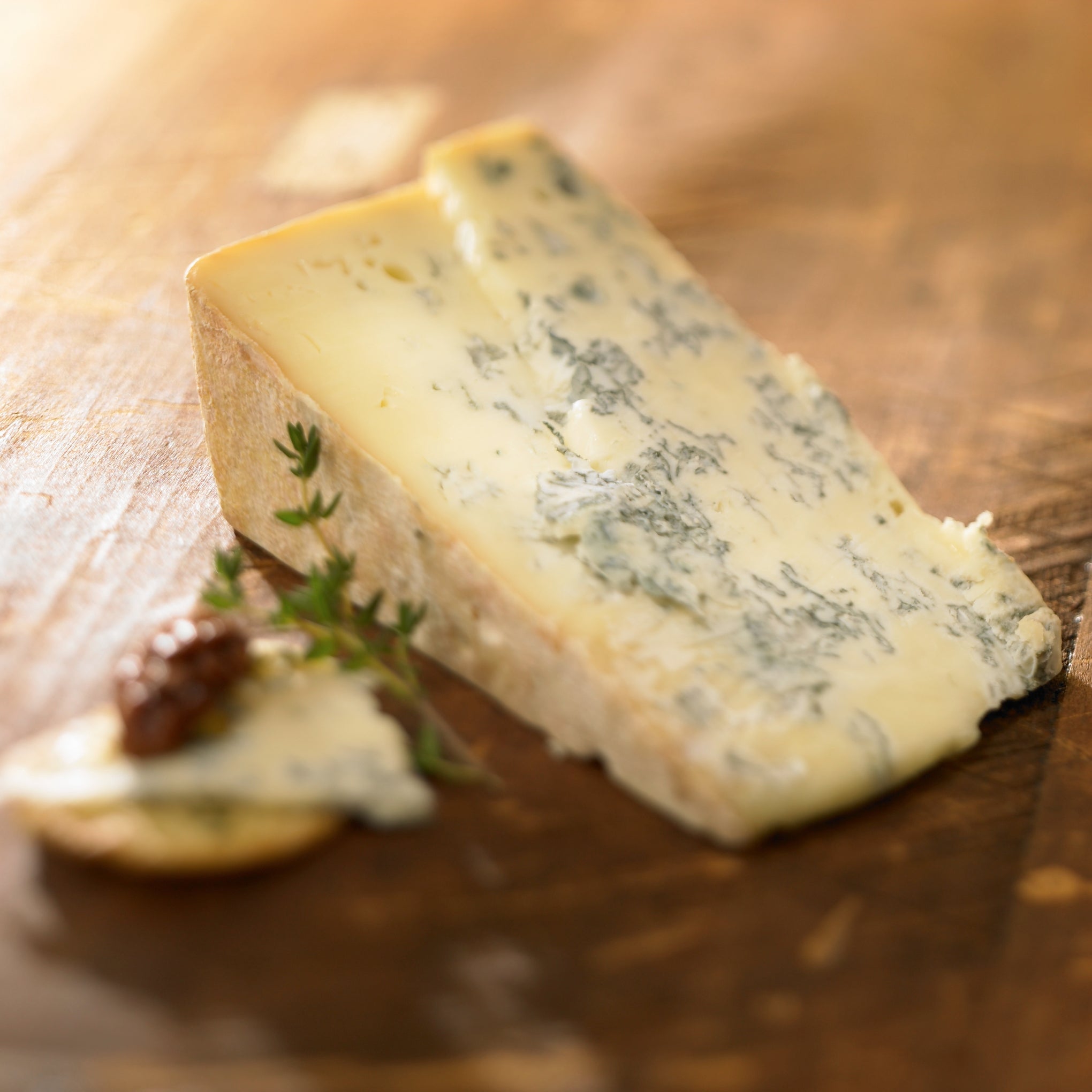 A wedge of Gorgonzola cheese showcasing its firm, crumbly texture and greenish-blue mold veins, served on a wooden board.