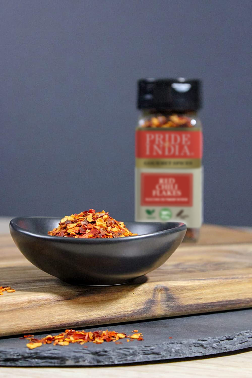 A jar of Pride Of India Gourmet Red Chili Flakes Hot, showcasing vibrant red crushed chili peppers, ideal for adding spice to dishes.