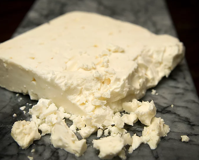 A block of Greek Style Traditional Feta cheese, showcasing its firm and crumbly texture, ideal for various dishes.