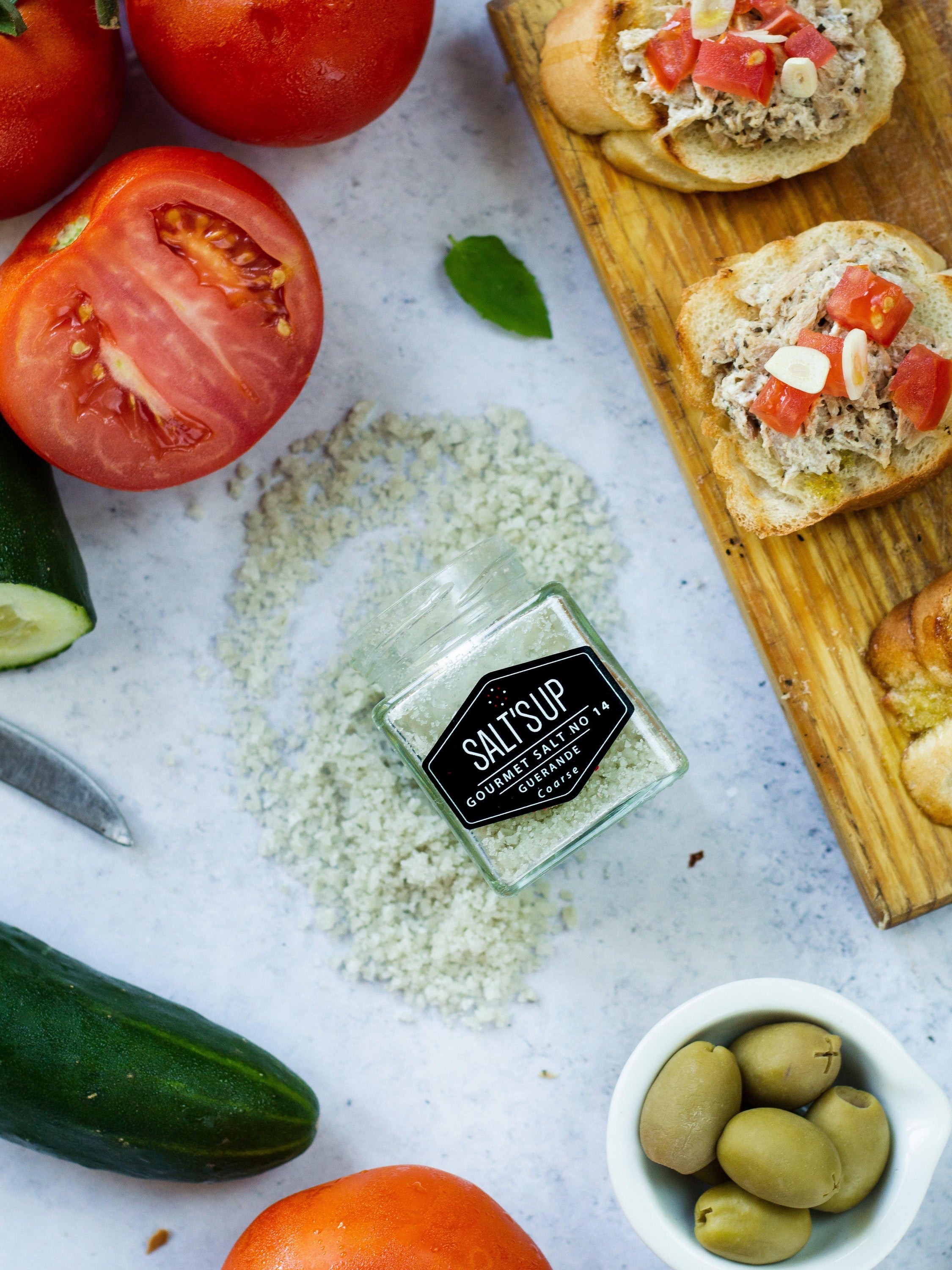 A jar of GUERANDE coarse salt showcasing its grey color and natural texture, perfect for seasoning dishes.