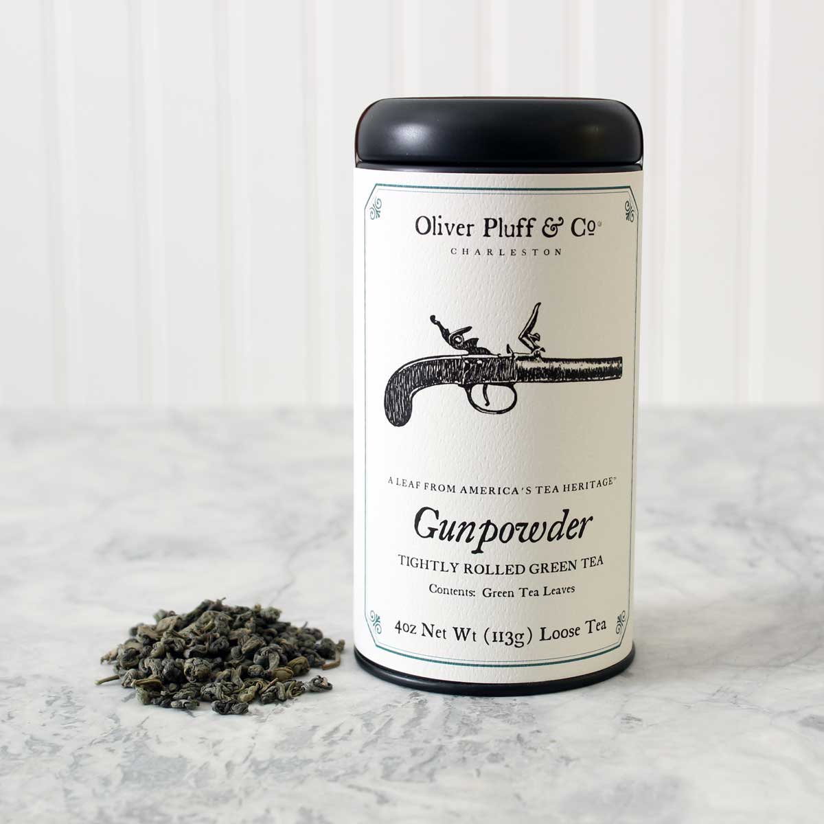 A matte black signature tea tin filled with Gunpowder Loose Tea, showcasing tightly rolled green tea leaves.