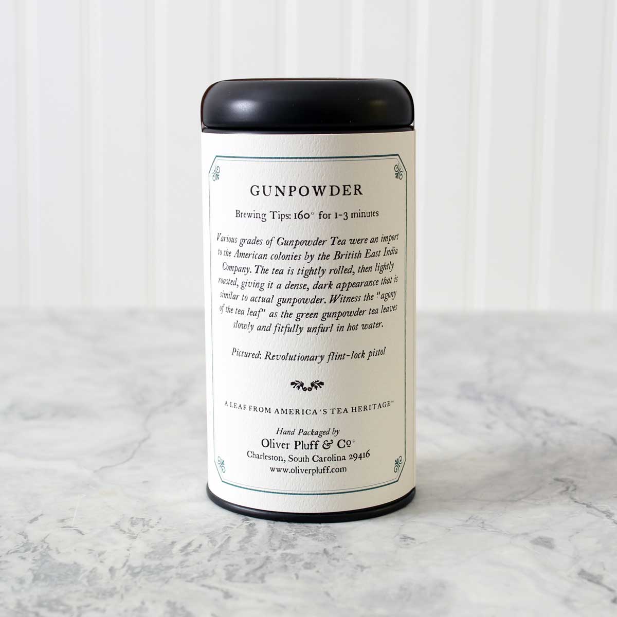 A matte black signature tea tin filled with Gunpowder Loose Tea, showcasing tightly rolled green tea leaves.