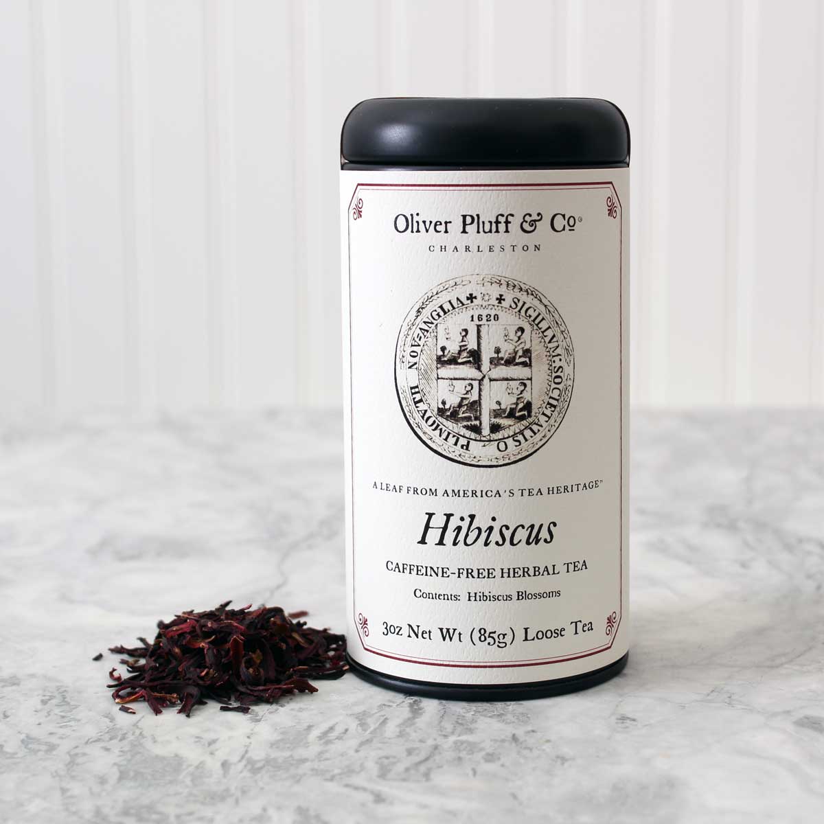 A matte black signature tea tin containing Hibiscus Loose Tea, showcasing vibrant red hibiscus flowers.