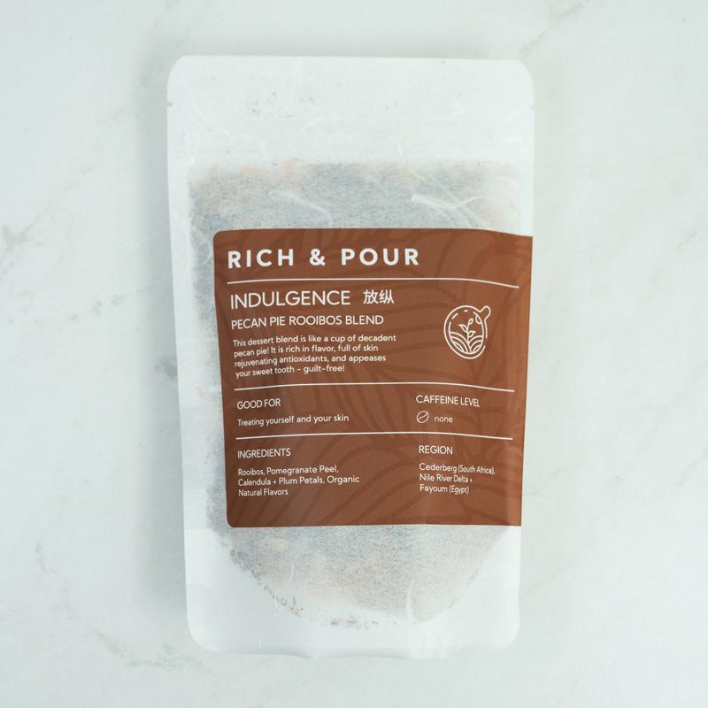 A cup of Pecan Pie Rooibos Blend tea with loose leaf ingredients and biodegradable packaging, showcasing its rich color and texture.