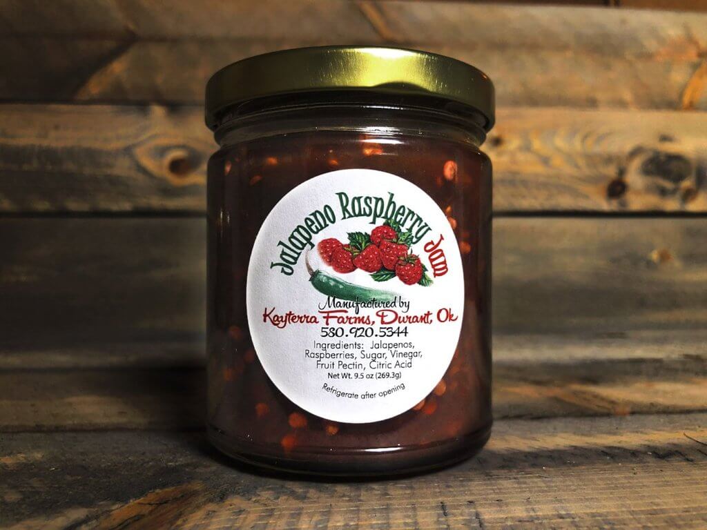 A jar of Jalapeno Raspberry spread showcasing its vibrant red color and jalapeno pepper pieces, perfect for adding sweetness and heat to dishes.