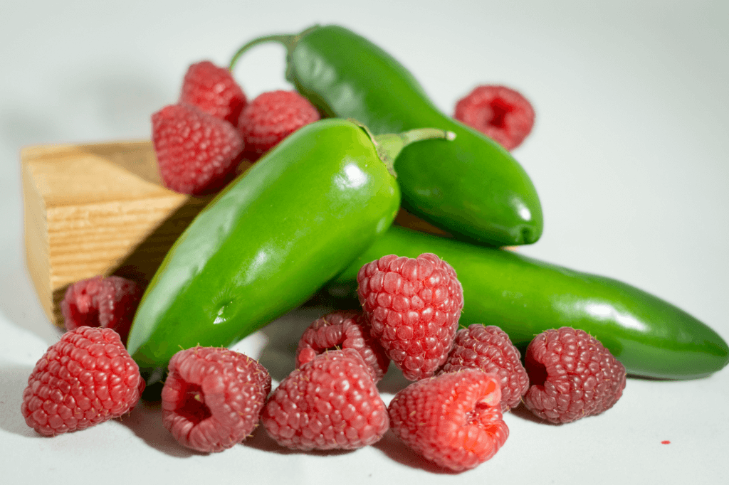 A jar of Jalapeno Raspberry spread showcasing its vibrant red color and jalapeno pepper pieces, perfect for adding sweetness and heat to dishes.