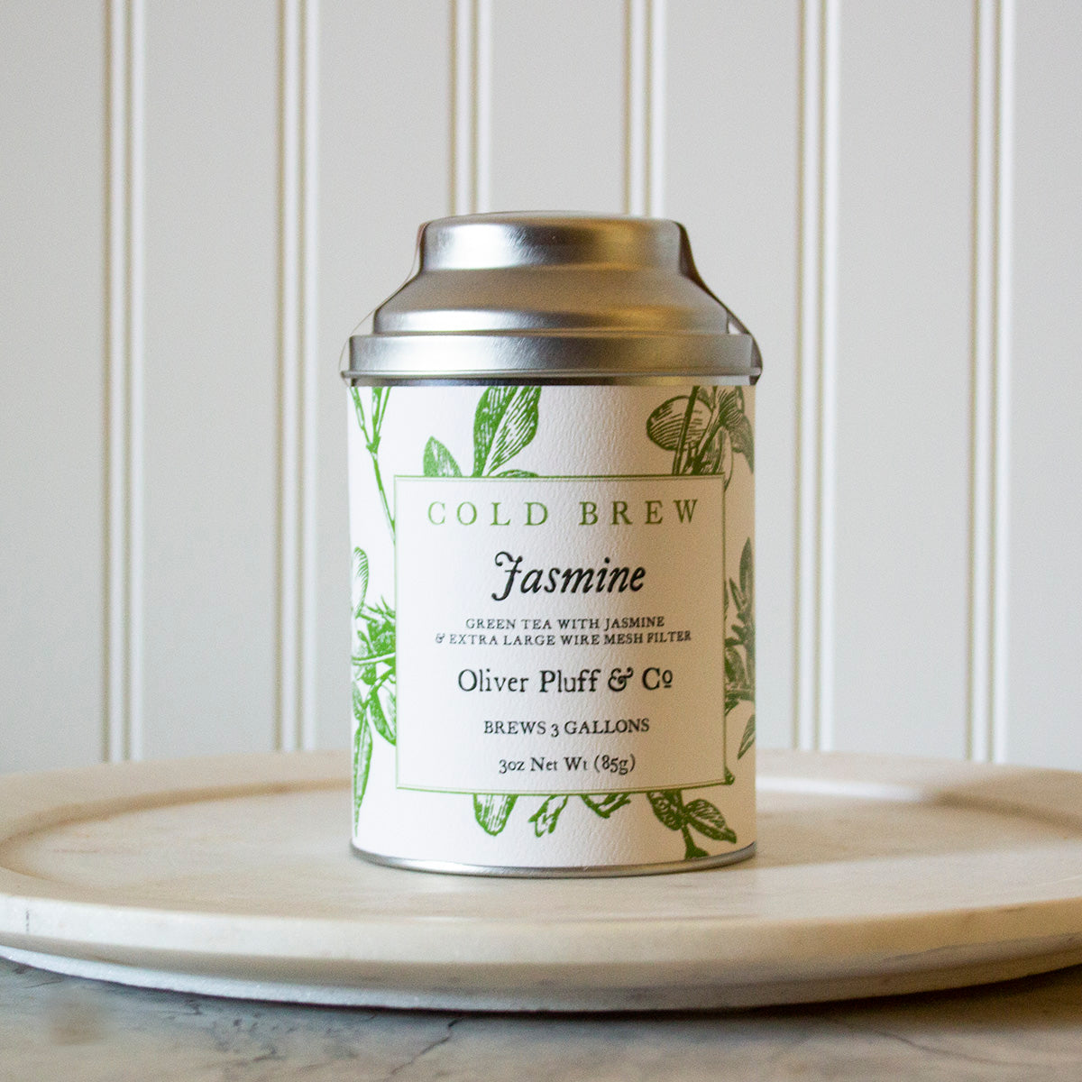 A tin of Jasmine Cold Brew tea with a large wire mesh brewing ball, showcasing the fragrant green tea blend.