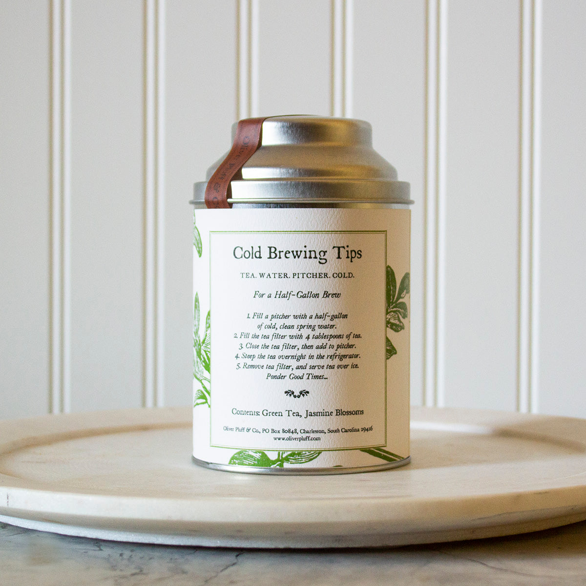 A tin of Jasmine Cold Brew tea with a large wire mesh brewing ball, showcasing the fragrant green tea blend.