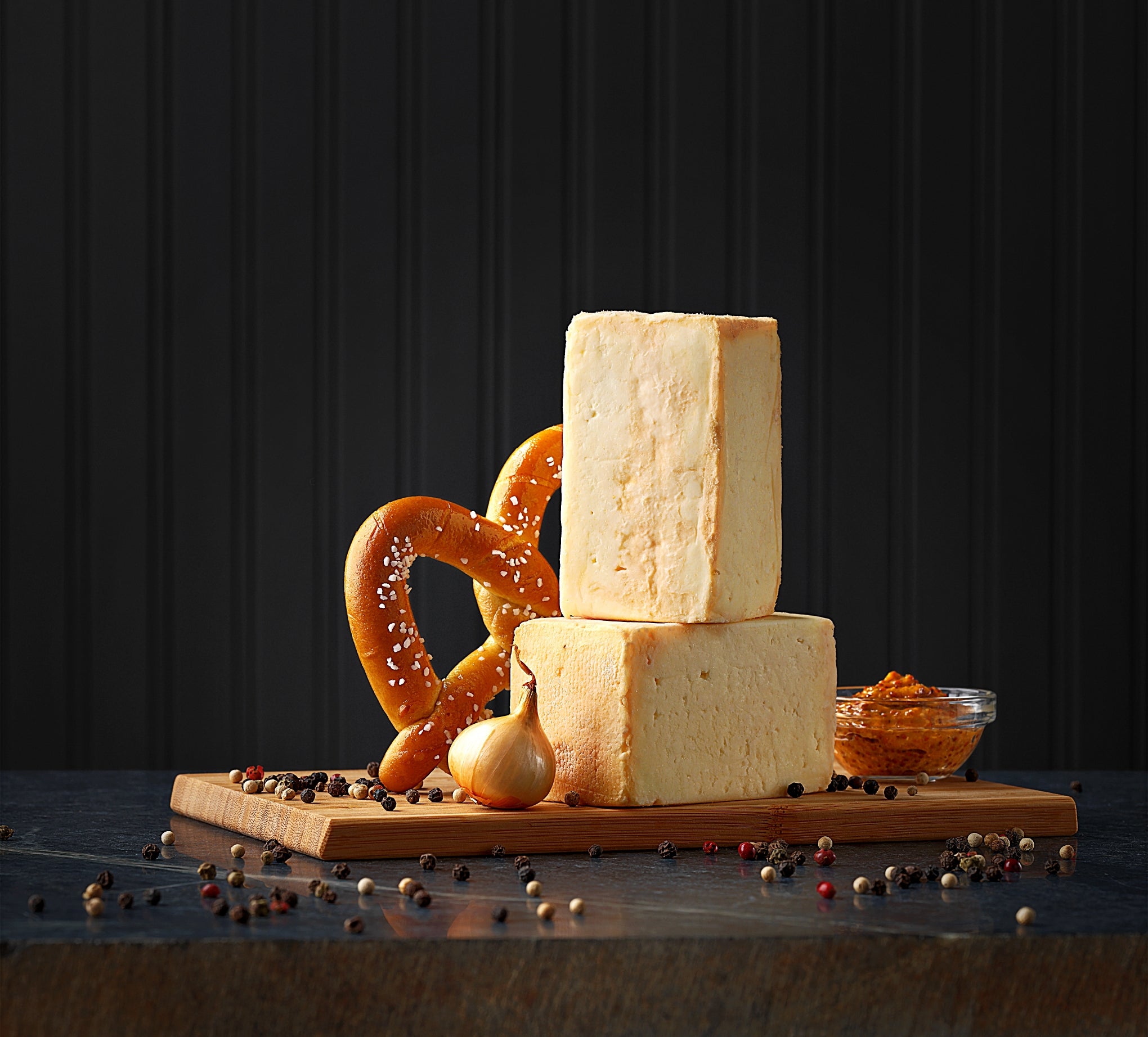 A round wheel of Limburger cheese with a creamy texture and strong aroma, displayed on a wooden cheese board alongside slices of bread and a glass of Zinfandel wine.