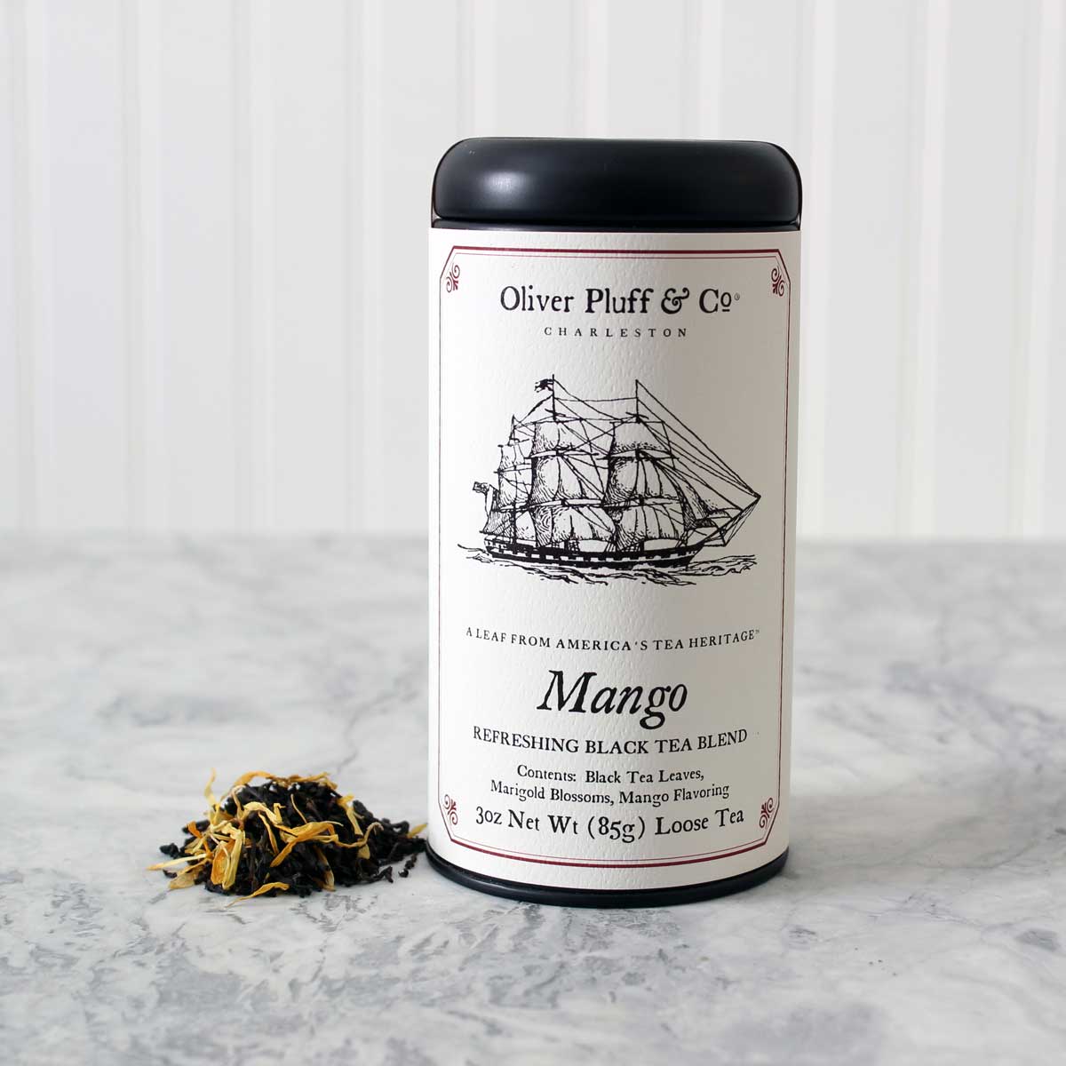 A matte black signature tea tin filled with loose leaf mango black tea, featuring vibrant marigold petals and a tropical mango flavor.