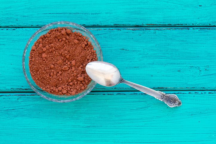 A bowl of Organic Peruvian Fair Trade Cacao Powder with cacao beans and a spoon, showcasing its rich brown color and fine texture.