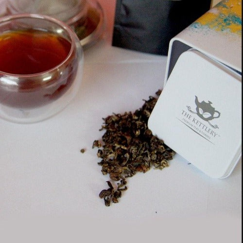 A cup of Organic Green Pearl Tea with fresh green tea leaves and a serene Darjeeling mountain backdrop.