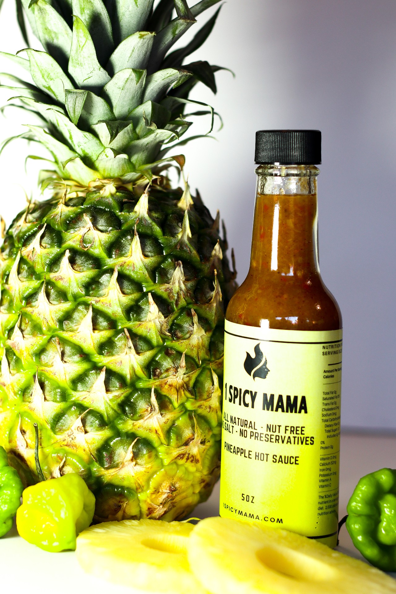 A bottle of Pineapple Hot Sauce featuring fresh pineapples and scotch bonnet peppers, showcasing its vibrant color and natural ingredients.