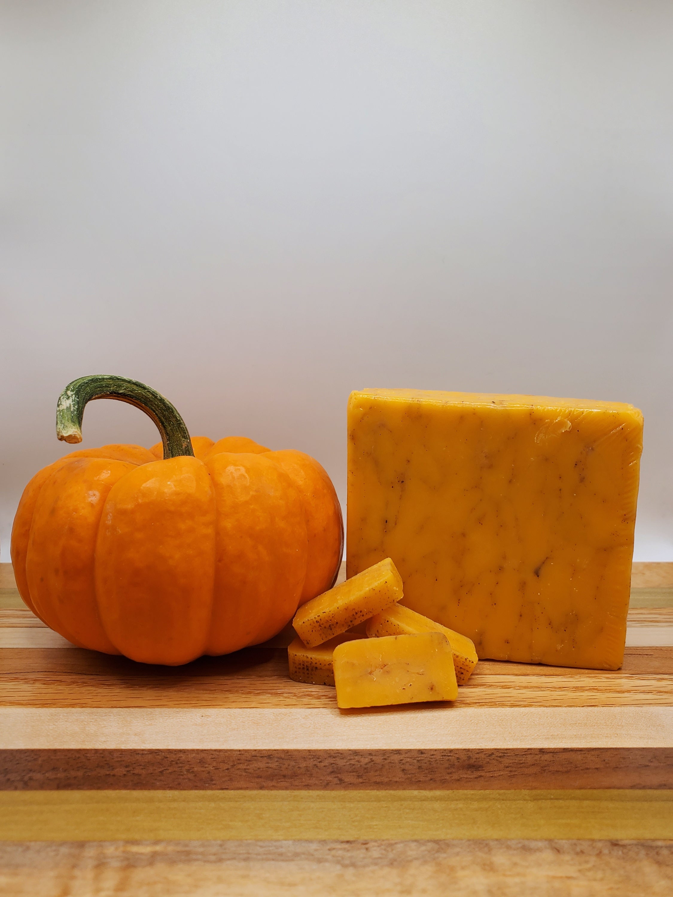 A block of Pumpkin Spice Cheddar cheese infused with autumn spices, showcasing its creamy texture and warm orange hue.