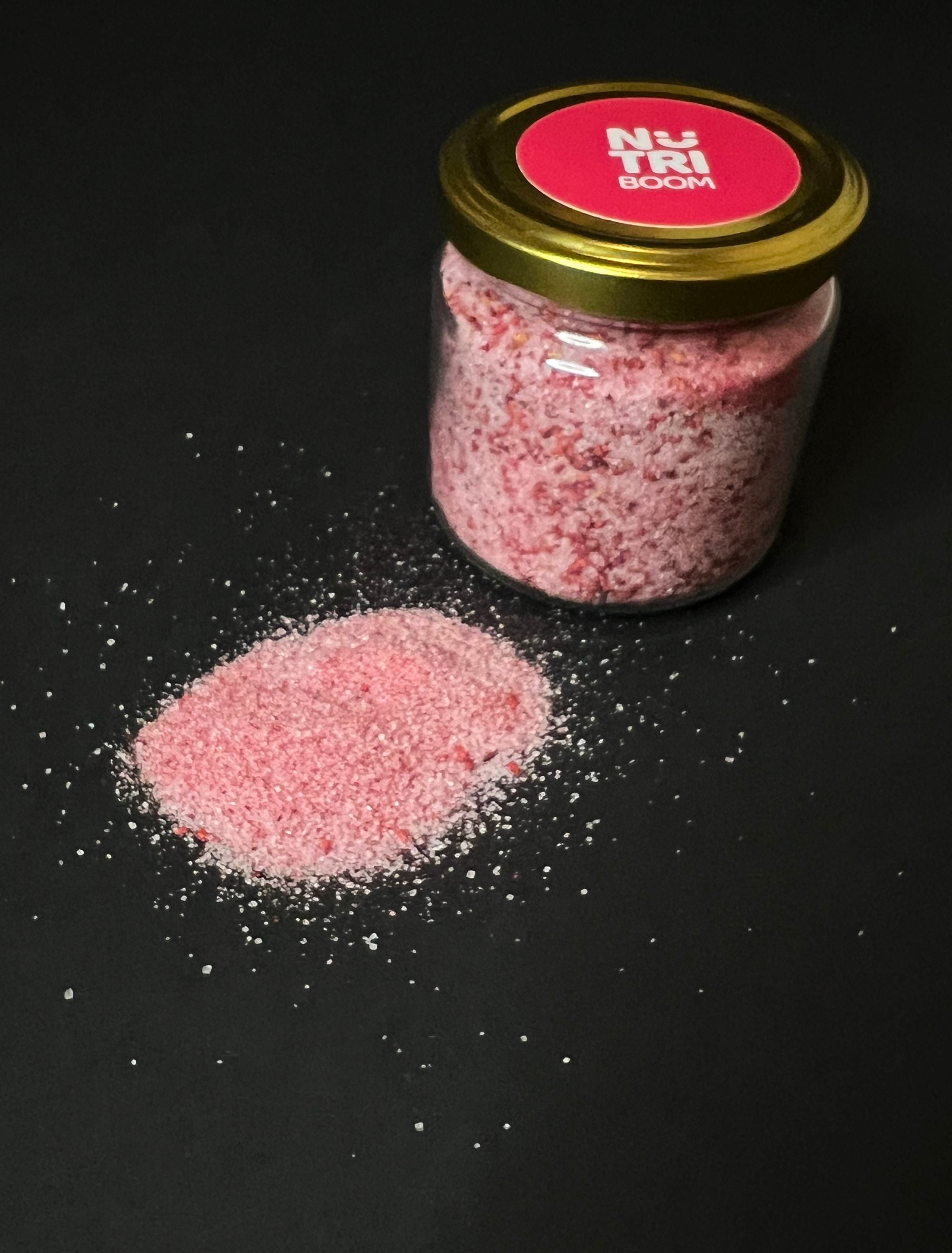 A glass jar filled with vibrant raspberry sugar, showcasing its rich pink color and fine texture, perfect for enhancing desserts.