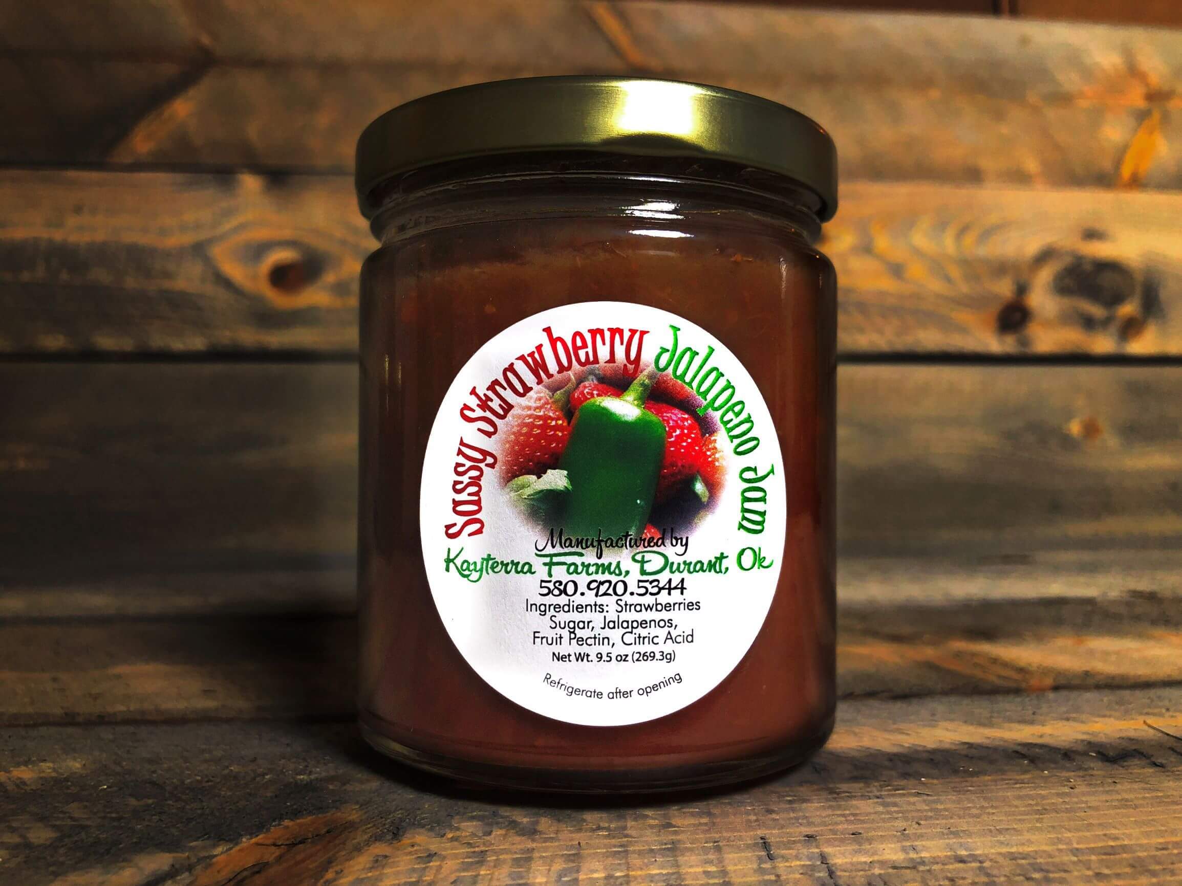 A jar of Sassy Strawberry Jalapeno jam showcasing its vibrant red color with jalapeno slices visible, perfect for adding a sweet and spicy flavor to dishes.