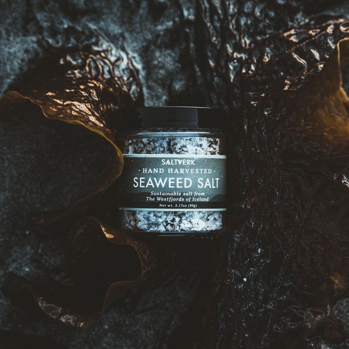 A jar of Seaweed Salt showcasing its rich texture and color, surrounded by fresh ingredients.