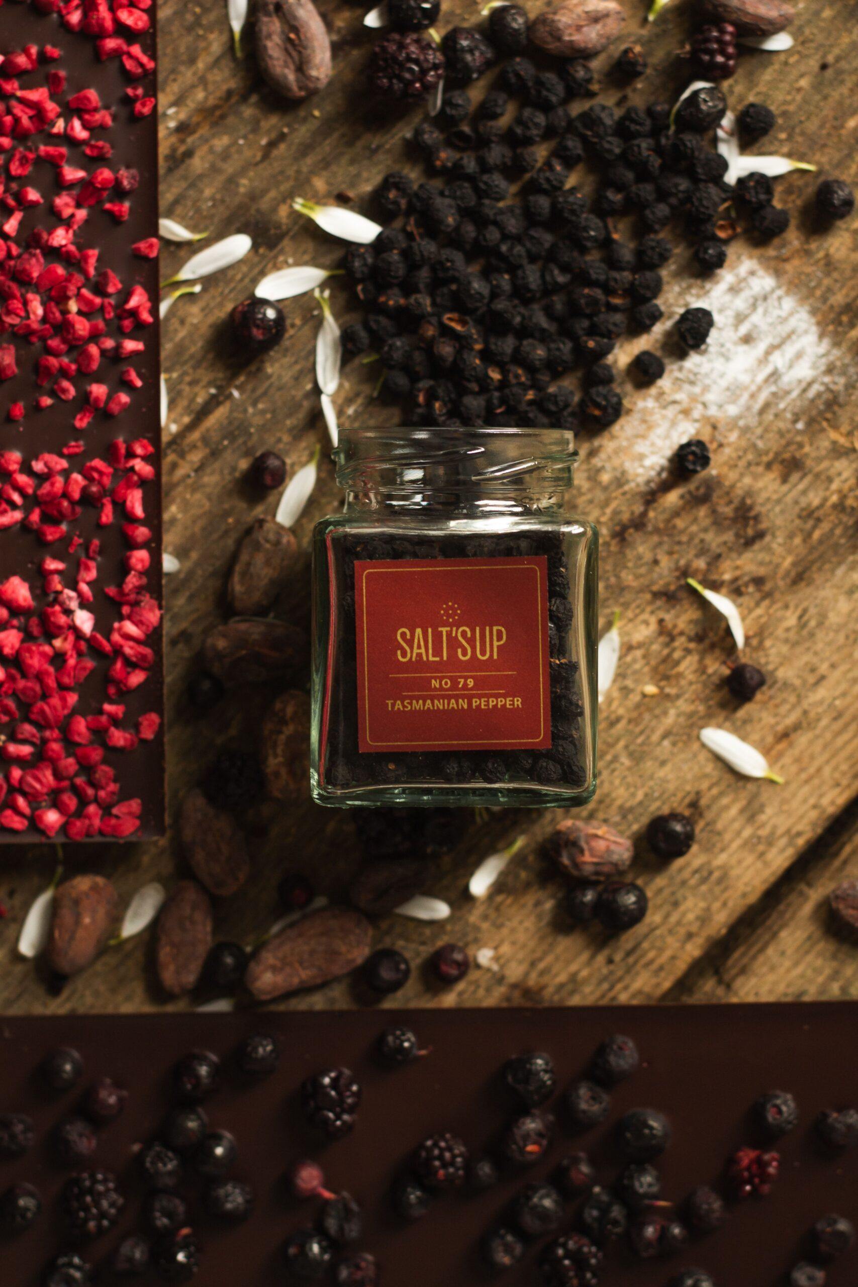 A jar of Tasmanian pepper ecopack showcasing its vibrant pink/purple hue and large berries, set against a rustic wooden background.