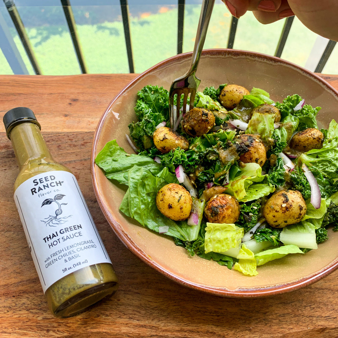 A bottle of Thai Green Hot Sauce featuring a vibrant green color, with fresh ingredients like lemongrass and lime in the background.