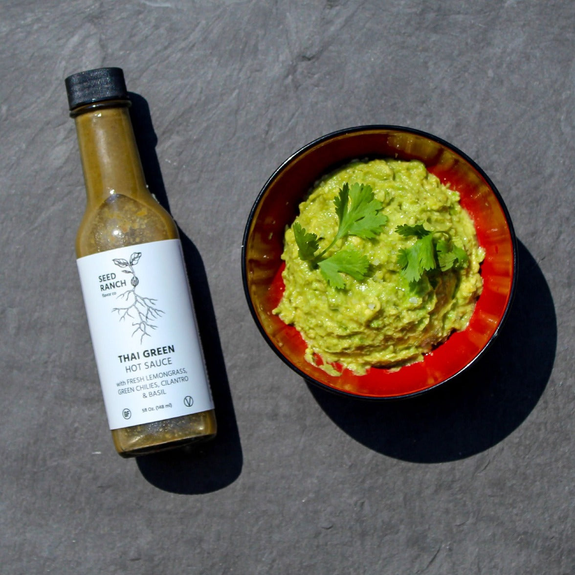 A bottle of Thai Green Hot Sauce featuring a vibrant green color, with fresh ingredients like lemongrass and lime in the background.