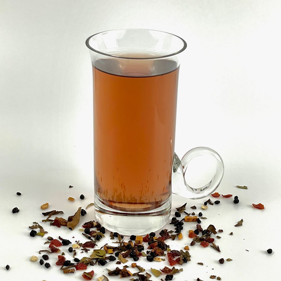 A vibrant cup of White Dragonfruit Berry Tea surrounded by tropical fruits and loose tea leaves, showcasing its exotic blend.