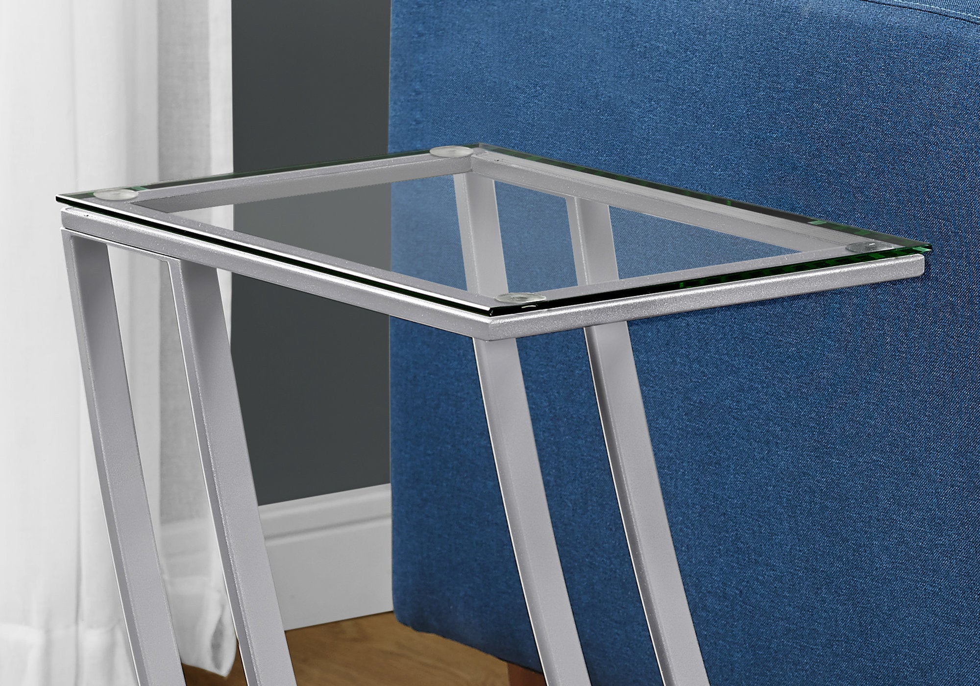 Stylish silver clear metal tempered glass accent table next to a sofa, showcasing its sleek design and elegant features.