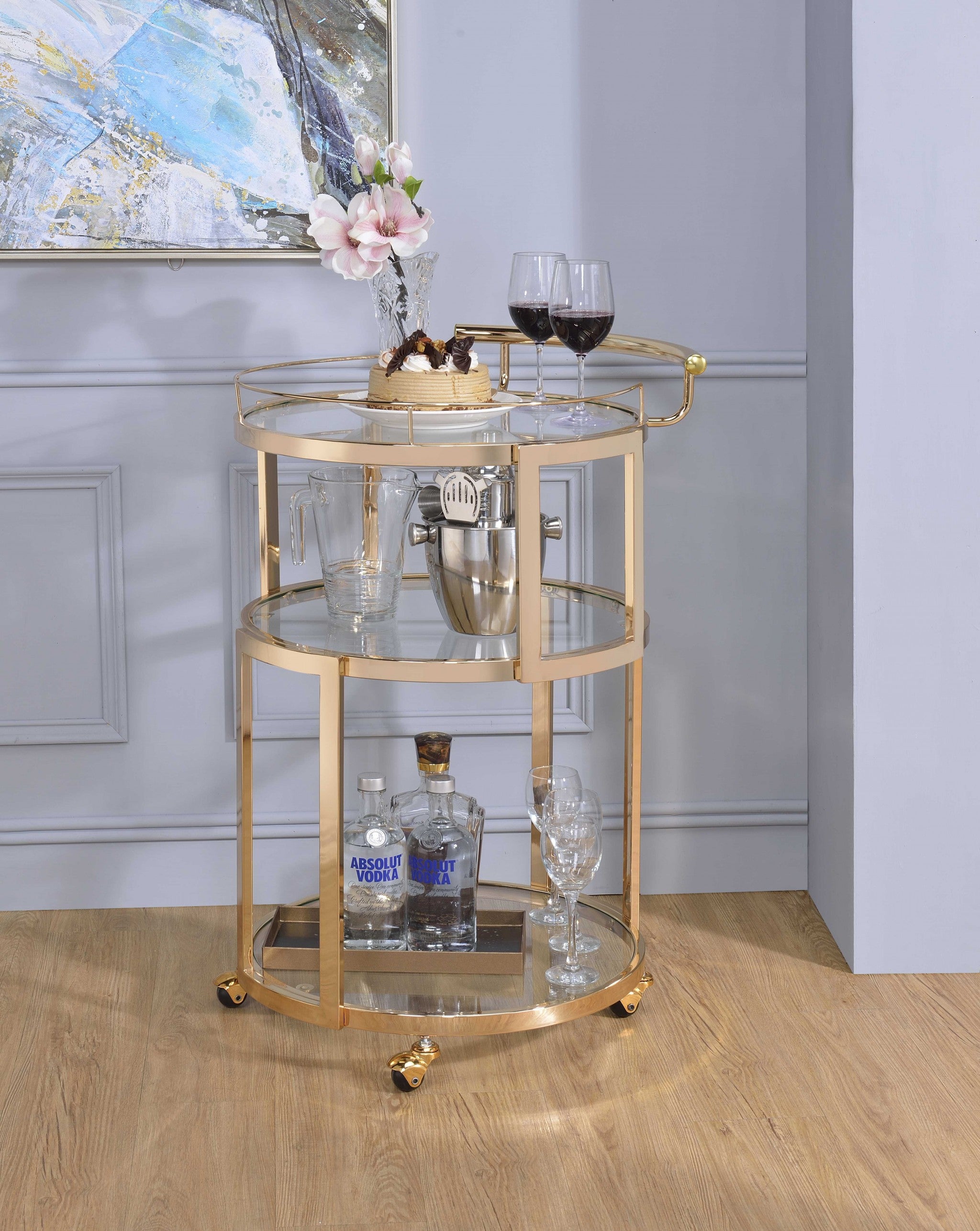 Elegant gold and clear glass serving cart with three shelves and caster wheels, perfect for serving meals and drinks.